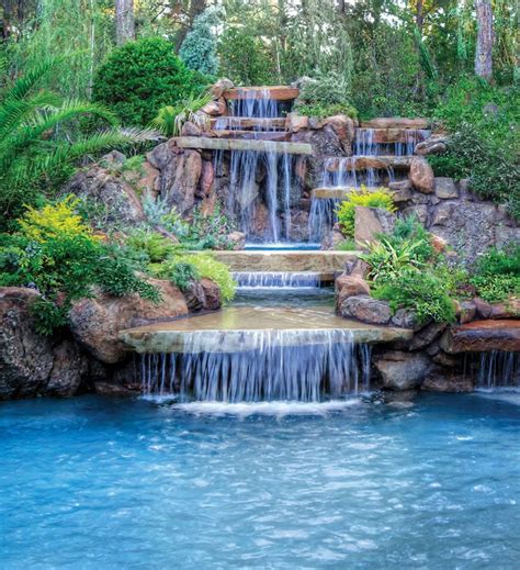 A 20-foot-high cascading waterfall with a two-sided spillway drops into a large spa that flows ...