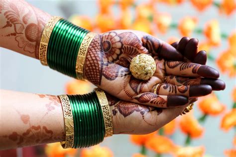 two hands with henna holding something in each hand and some orange flowers behind them