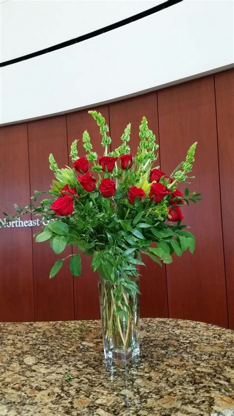 a vase filled with red roses sitting on top of a table next to a wall