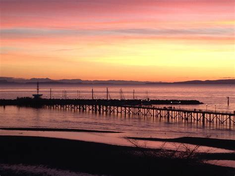 the sun is setting over an ocean with a pier in the foreground