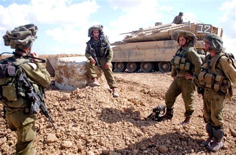 Israeli soldiers wearing Mitznefet helmet cover. Merkava Mk 4 tank visible at the background ...