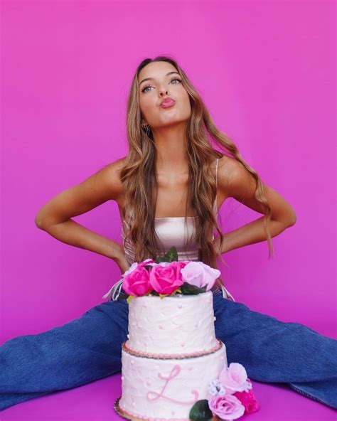 a woman sitting in front of a white cake with pink flowers on it and ...