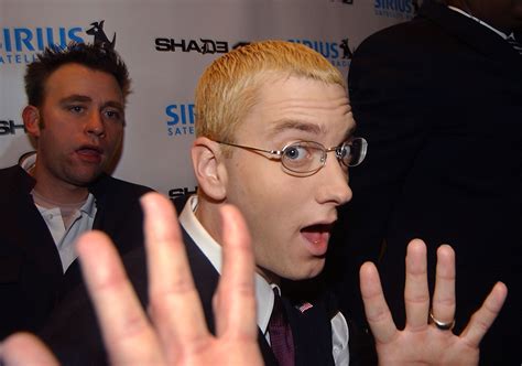 a man in glasses making a face with his hand up to the camera while another man looks on