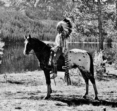 an old black and white photo of a native american man on a horse next to a lake