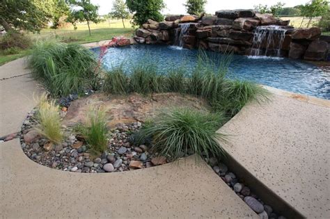 Salt finish concrete pool decking surrounds a river rock planting bed. By: Outdoor Signature in ...