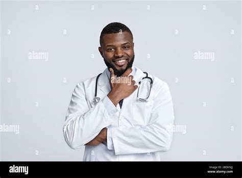 Cheerful black doctor touching his chin and smiling at camera Stock Photo - Alamy