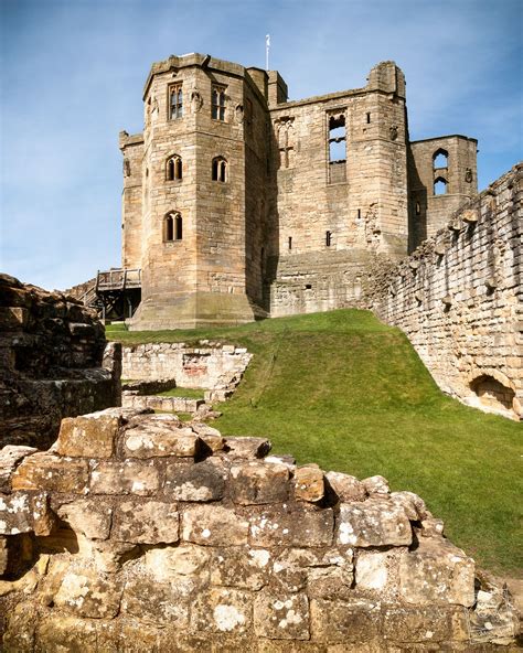 an old castle sitting on top of a lush green field next to a stone wall