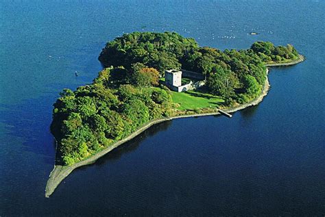 an island in the middle of water surrounded by trees and grass, with a house on it