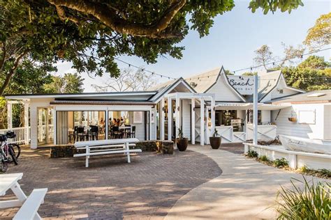 a white building with lots of tables and benches in front of it on a sunny day