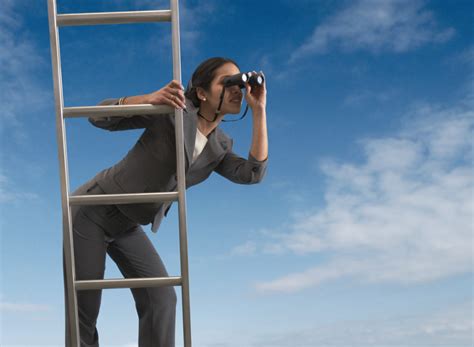 Businesswoman standing on a ladder looking through binoculars ...