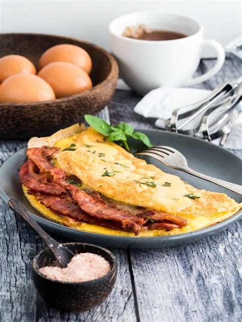 an omelet with bacon and eggs on a plate next to a bowl of eggs