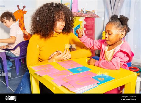 Little black girl point cursive letter learning with tactile cards helped by teacher in nursery ...