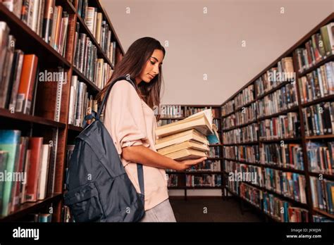 Young female student carrying lots of books in the college library. Caucasian student reading ...