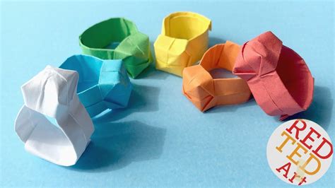 an origami ring is sitting on a blue surface next to several different colored paper rings