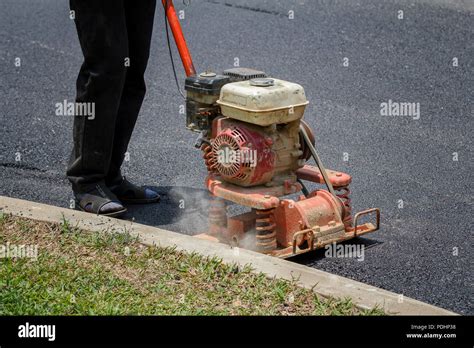 Worker uses vibratory plate compactor compacting asphalt at road repair ...