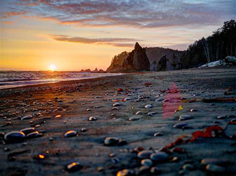 the sun is setting at the beach with rocks and pebbles on the sand in front of it