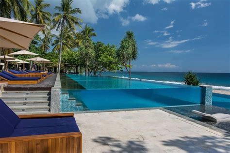 an outdoor swimming pool with lounge chairs and umbrellas next to the ocean on a sunny day