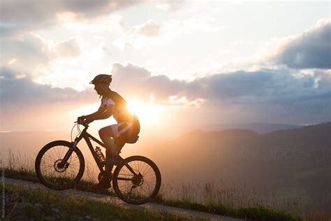 Man Riding A Bike Uphill Against Sunset Sky | Stocksy United