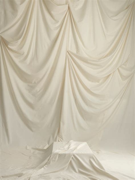 an empty photo studio with white cloth draped over the top and bottom wall, in front of a plain ...