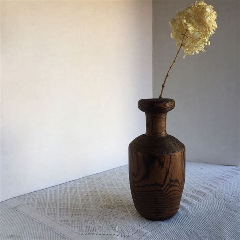 a wooden vase with a yellow flower in it sitting on a white table cloth ...