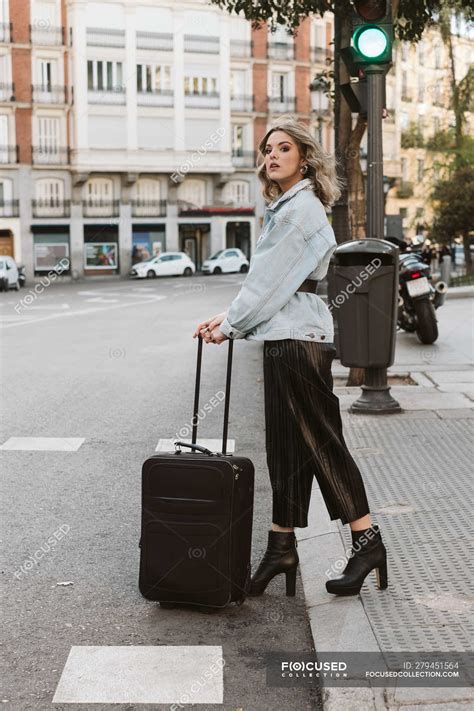 Stylish young woman with suitcase looking away while crossing city street — trip, travel - Stock ...