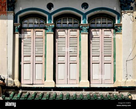 Traditional shop house exterior with pink wooden louvered shutters, arched windows and cream ...