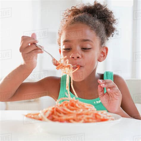 Mixed race girl eating spaghetti - Stock Photo - Dissolve