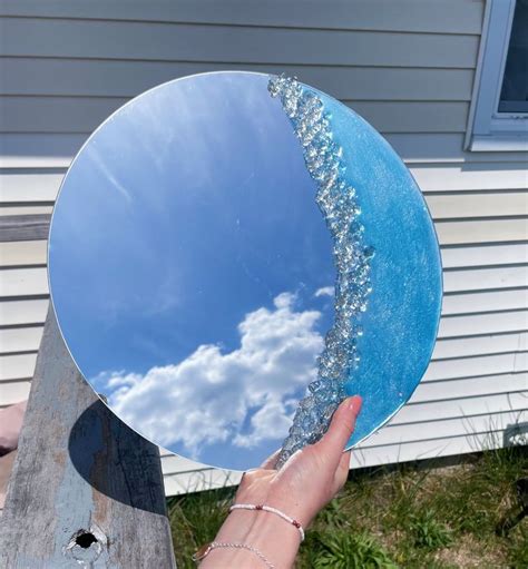 a hand holding up a mirror with the reflection of clouds and sky in it's center