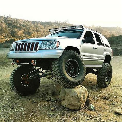 a white jeep parked on top of a rock in the middle of a dirt field