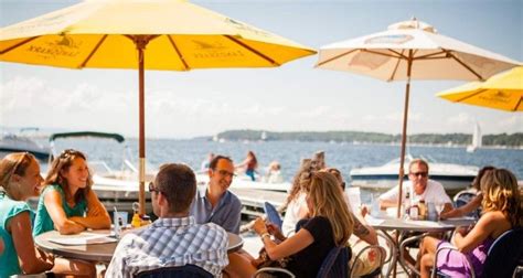 a group of people sitting at tables with umbrellas on the water in ...