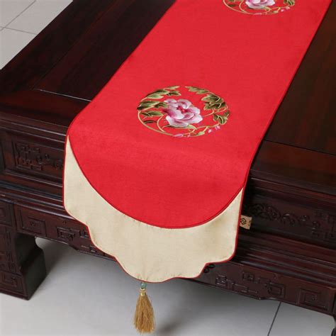a red table runner with gold trimmings and flowers on the edge, along with a tassel