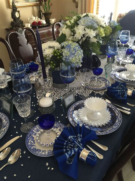 the table is set with blue and white dishes, silverware, and vases