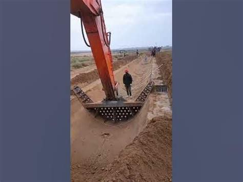 an excavator in the middle of a dirt field next to a man