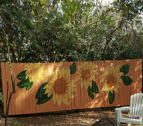 a wooden fence with sunflowers painted on it and two chairs in the foreground