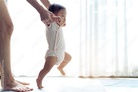 Asian baby taking first steps walk forward on the soft mat. Happy little baby learning to walk ...