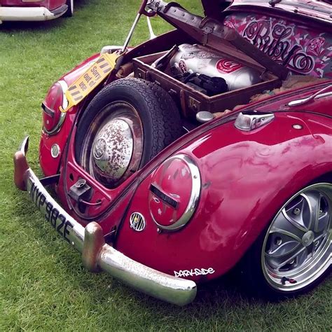 an old vw bug is parked on the grass with its hood up and engine open