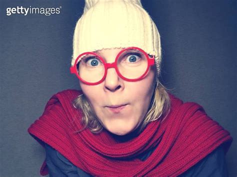 Funny young woman in red round glasses, red knitted hat and scarf grimaces looking at the camera ...