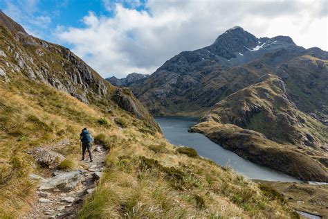 a person hiking up a mountain trail near a body of water in the distance with mountains behind them