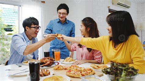 Happy young friends group having lunch at home. Asia family party eating pizza food and laughing ...