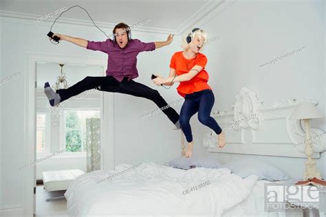 Playful couple jumping on bed and listening to music with mp3 player ...