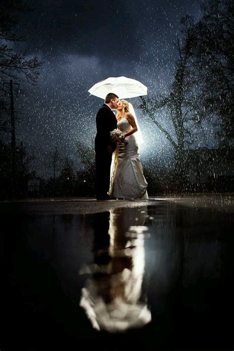 a bride and groom standing under an umbrella in the rain at night with their reflection on the water