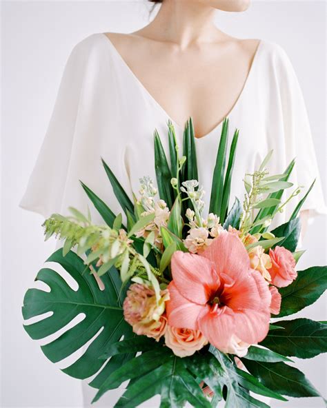 a woman wearing a white dress holding a bouquet of flowers and palm fronds