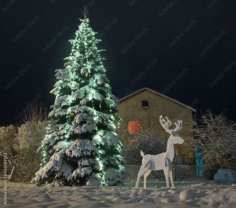 Snow covered outdoor Christmas tree with green lights and white ...