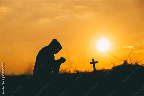 Man kneeling down and praying with the cross at sunset background. christian silhouette concept ...