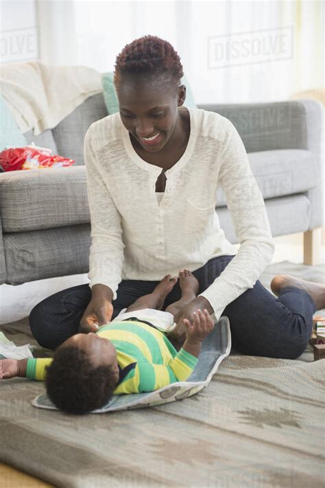 Black mother changing diaper of baby boy in living room - Stock Photo - Dissolve