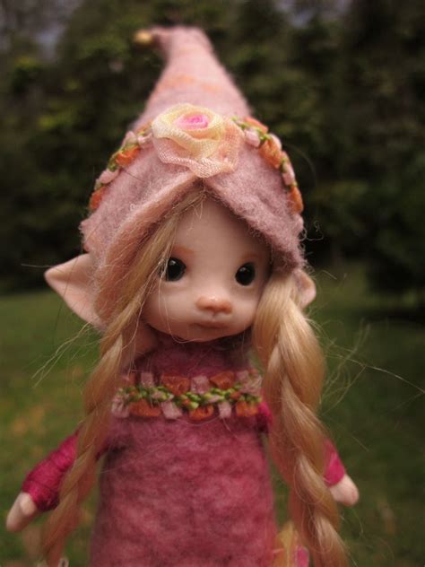 a doll with long blonde hair wearing a pink hat and dress, standing in the grass