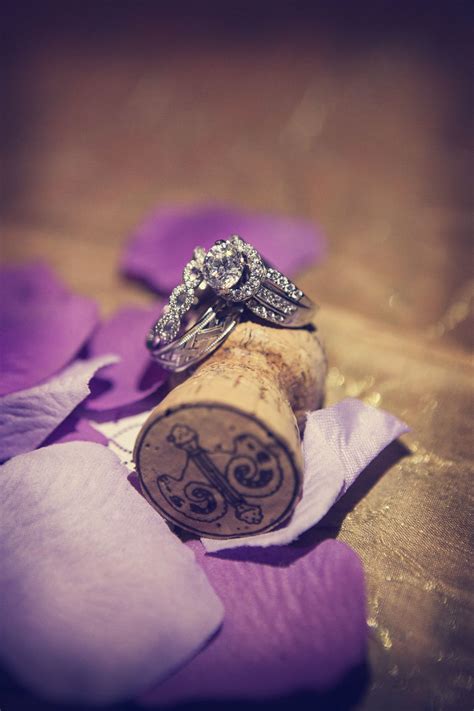 two wedding rings sitting on top of a wine cork next to purple petals and flowers