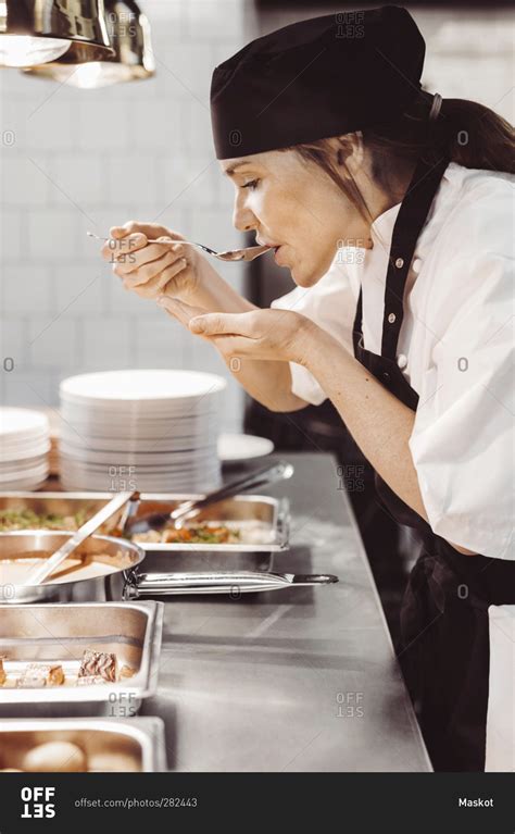 Side view of female chef tasting food at commercial kitchen stock photo - OFFSET