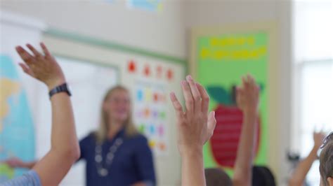 Teacher gives lesson in school classroom and students raise hands, rack ...