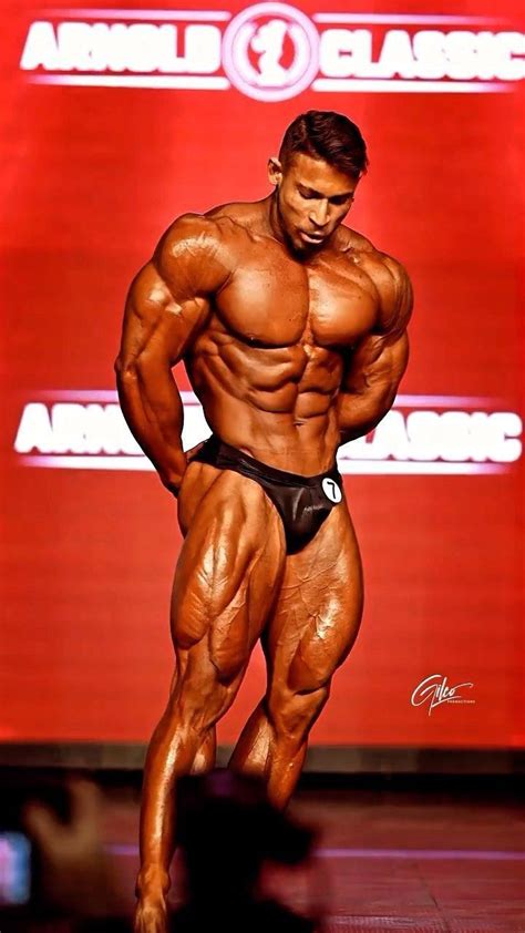 a male bodybuilding competitor posing for the camera on a stage with his hands in his pockets